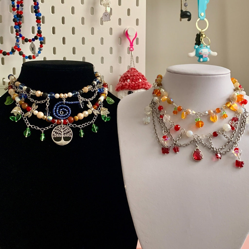 Four necklaces on two stands, two of them on each stand. The necklaces are beaded, are have various Halloween and fall elements.