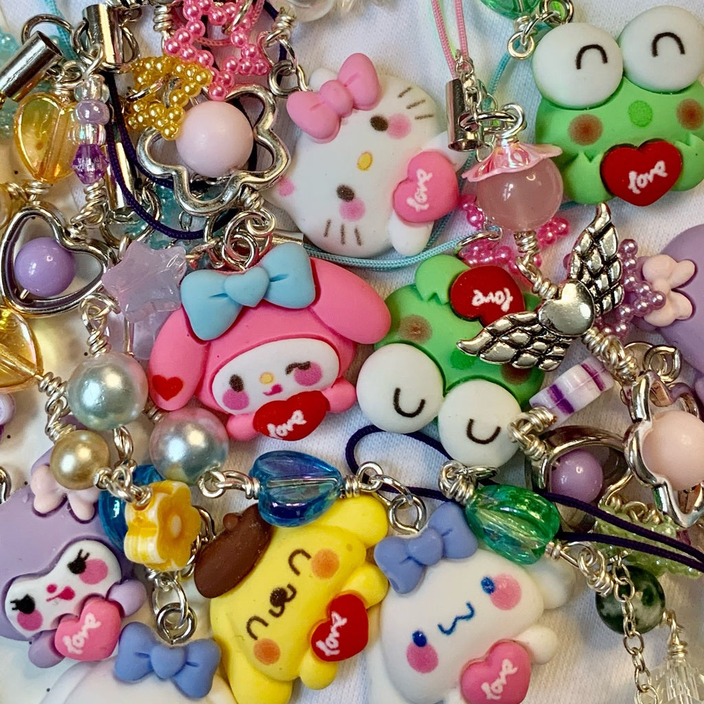 Sanrio phone charms lying flat. Characters pictured: Hello Kitty, My Melody, Kuromi, Pompompurin, Keroppi, Cinnamoroll