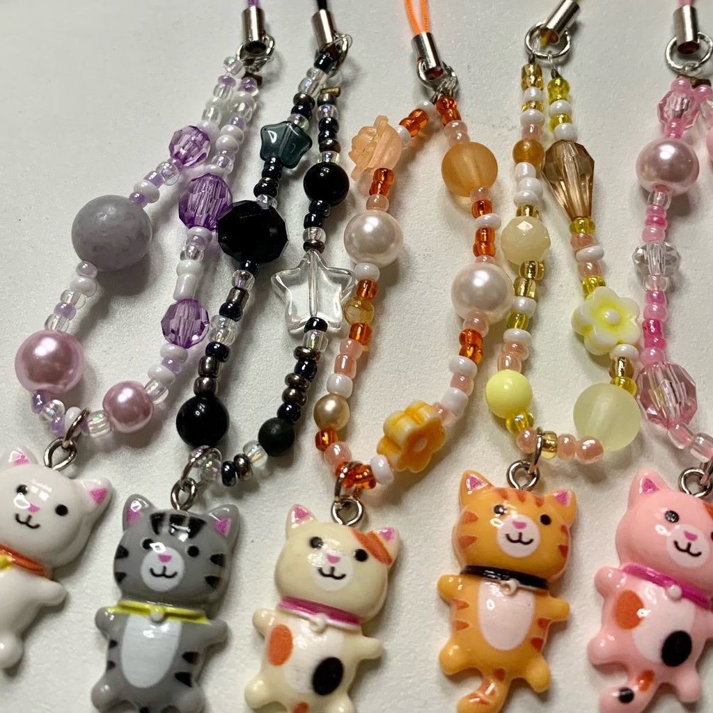 Five differently coloured cat phone charms lie flat.